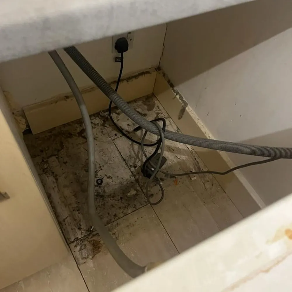 Floor behind an appliance covered in dirt and debris