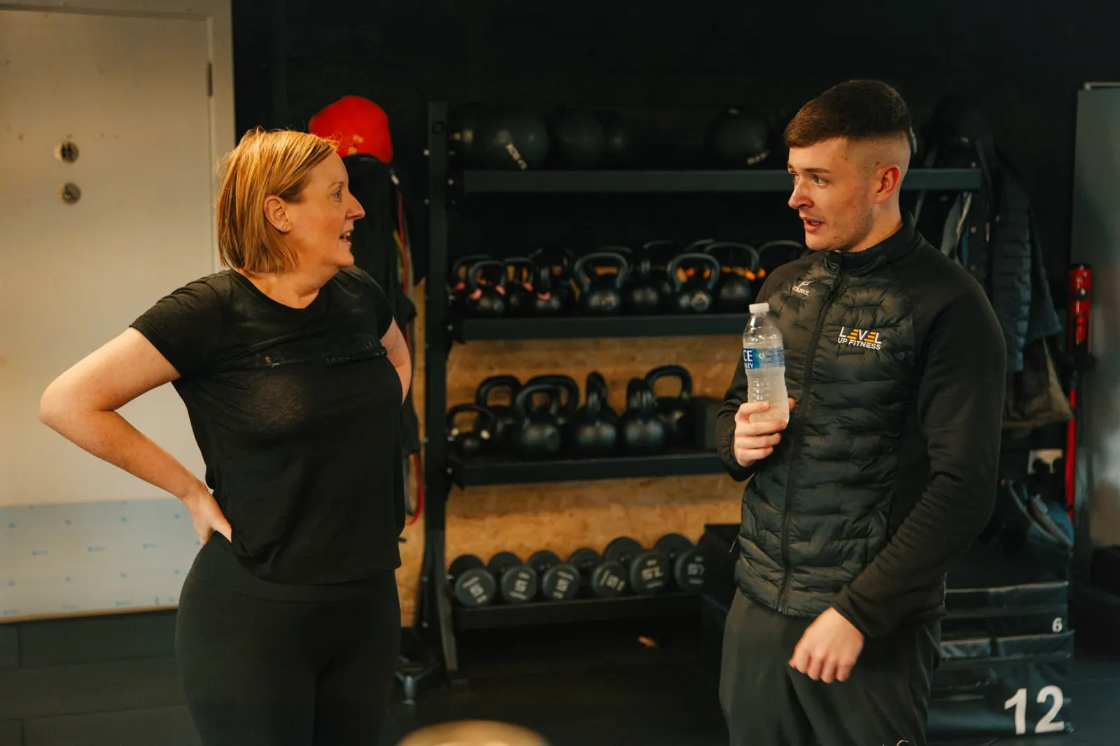A coach and a member talking by the kettlebell rack at Level Up Fitness