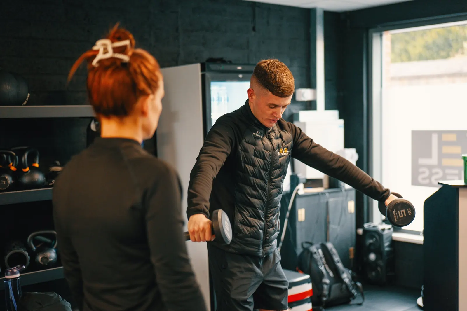 A Level Up Fitness coach showing a member how to do a dumbbell raise