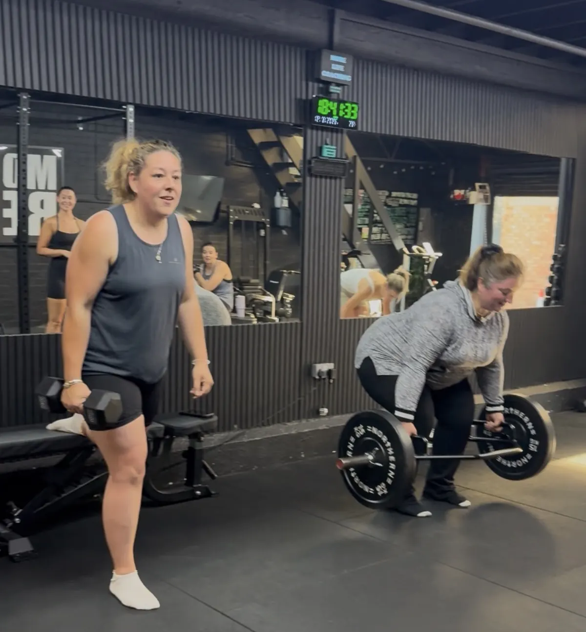 Two members smiling during a deadlift and dumbbell session at More Life Coaching